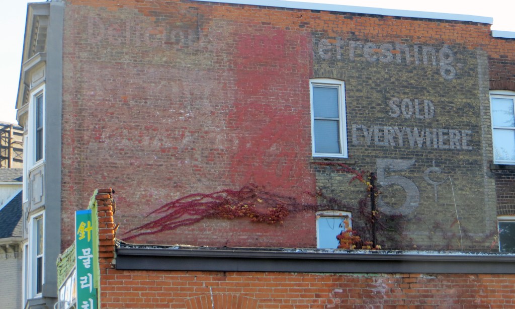 Large very faded Coca-Cola ad on exterior brick wall.