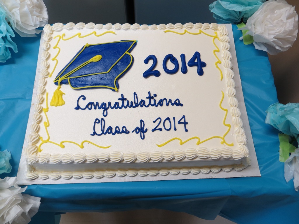 Rectangular cake with mostly white frosting and a blue graduation also cap done in frosting.