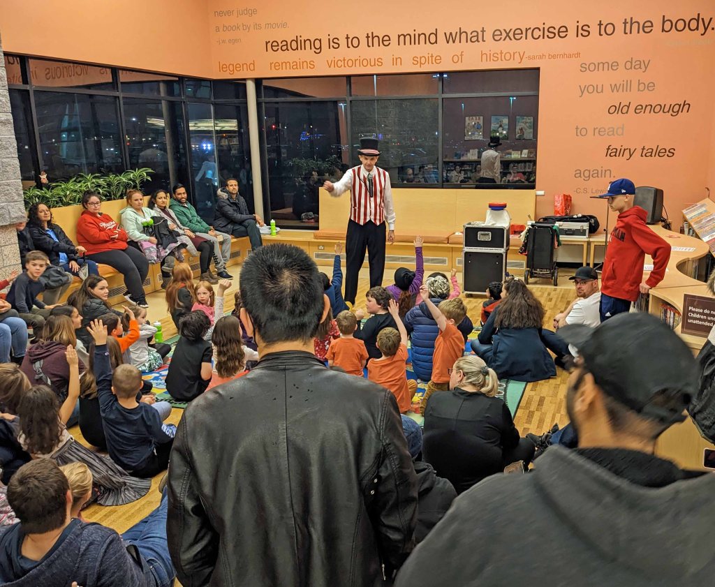 Magician Owen performing for a large family audience at a library.