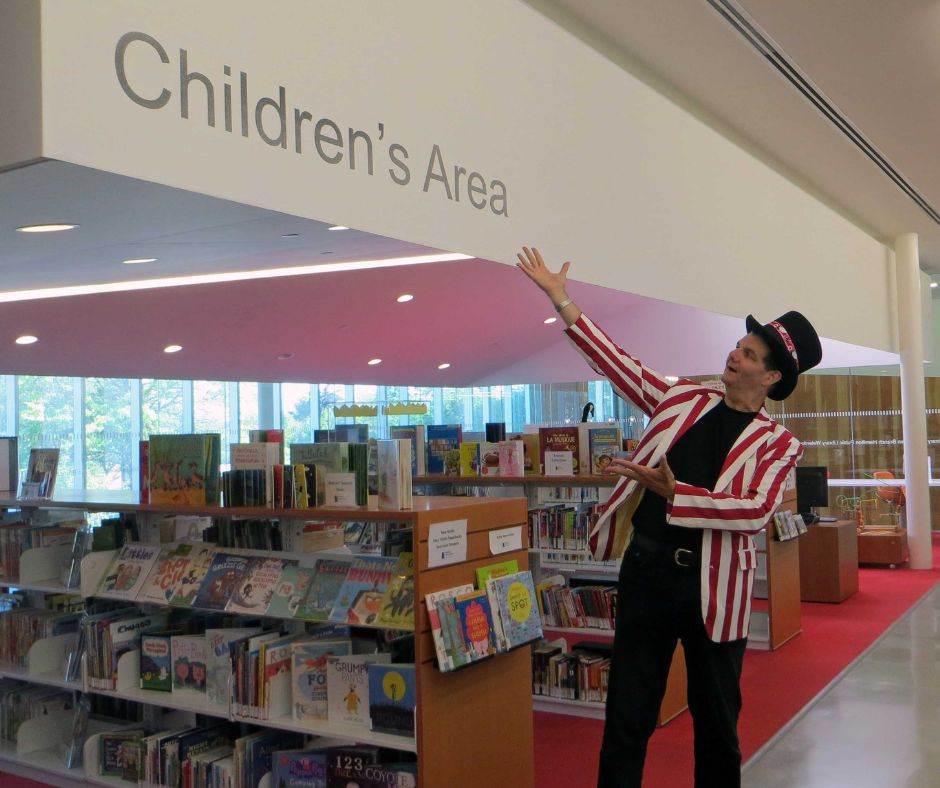 Magician Owen gesturing to sign that reads Children's Area inside the Waterdown library.