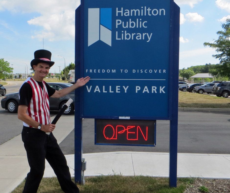 Magician Owen standing next to the Valley Park branch library sign.