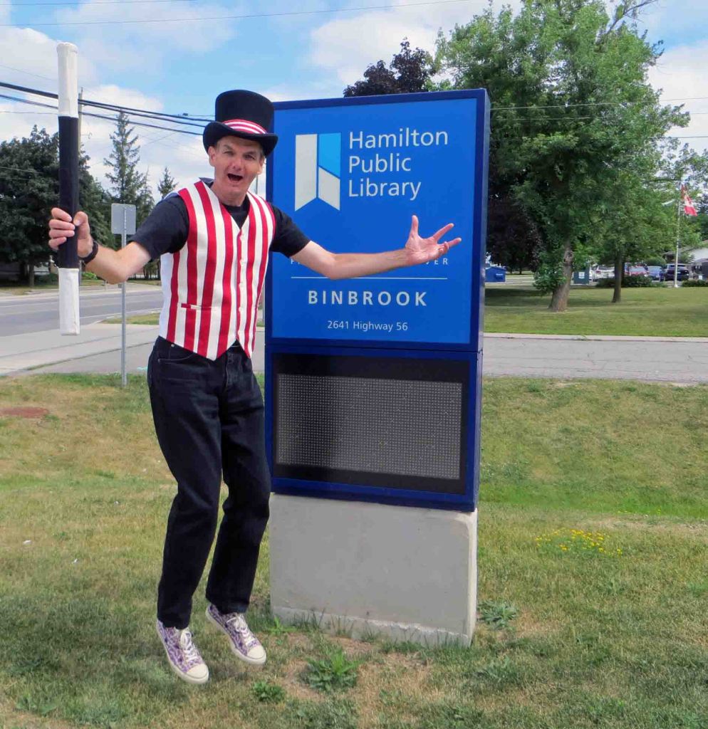 Magician Owen next to Binbrook library branch outdoor sign.