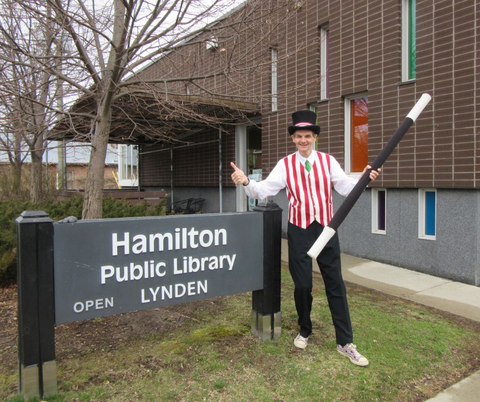 Magician Owen in costume next to the Lynden Library sign in front of the branch.