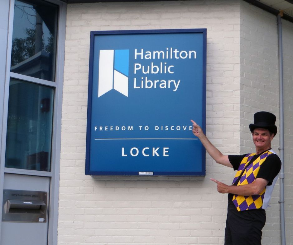 Magician Owen outside the Locke Street library branch gesturing at its signage.