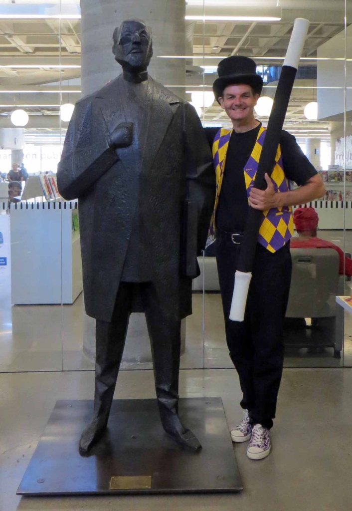 Owen in costume standing next to sculpture of librarian in entrance to Central Branch library.